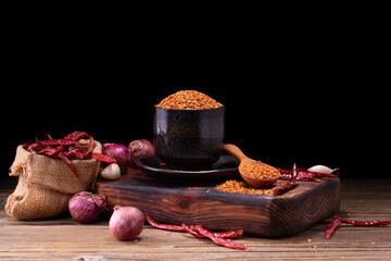 Chili powder in black bowl and wooden spoon with garlic, shallots and spicy spice mix. Asian food ingredients arranged on wooden table.