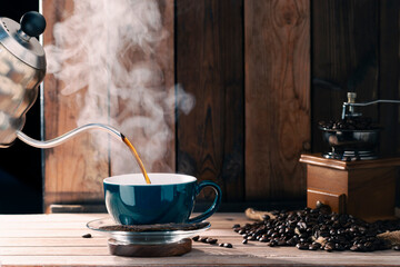 Black coffee is poured into a green coffee cup. Roasted coffee beans are on the table in a morning light atmosphere, against a backdrop of dark wood walls.