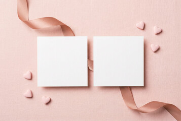 Top view photo of valentine's day decorations curly silk ribbon small hearts and two paper cards on isolated pastel pink background with copyspace