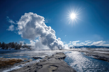 Erupting geyser plume with windblown steam drifting across rugged geothermal basin