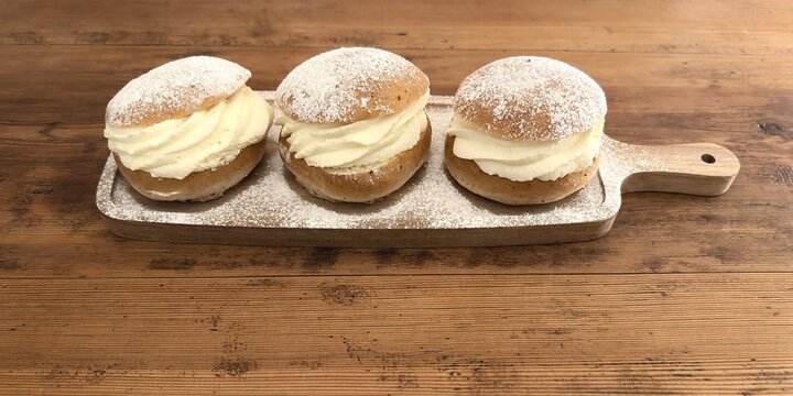 Three Swedish semla buns on rustic wooden table &ndash; traditional cream pastries for Fettisdagen (Shrove Tuesday)