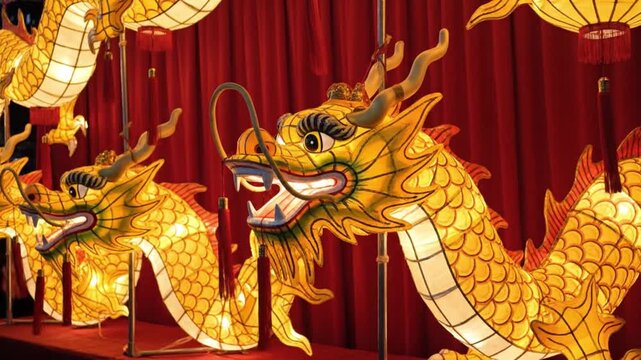 Golden dragon lanterns displayed at a festival or celebration, with red curtains in the background