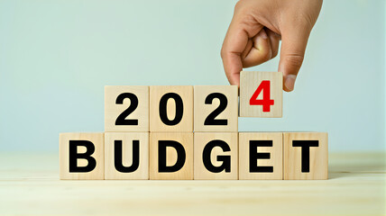 A hand carefully places wooden blocks to form '2024 BUDGET', representing meticulous financial planning and economic strategy for the upcoming fiscal year