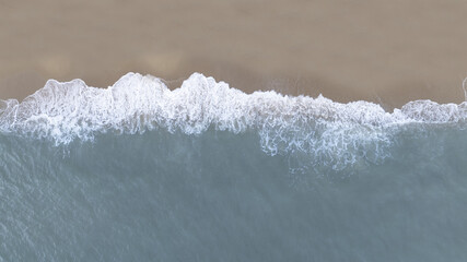 Aerial top view of ocean waves gently meeting sandy beach, perfect for background, commercial design, and nature concepts.