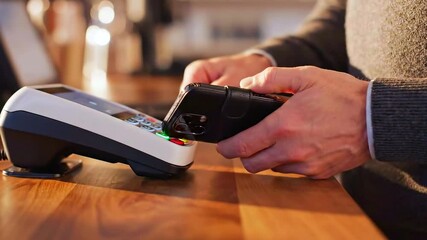 customer taps smartphone on terminal at wooden cafe counter for contactless payment warm ambient lighting, closeup of hands and device, nfc transaction approval, quick secure checkout, - Powered by Adobe