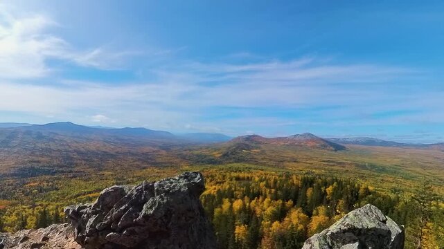 A panoramic view from a rocky outcrop overlooking the vast, forested landscape of the Southern Urals in Russia during the vibrant autumn season. The trees display brilliant yellow and golden foliage u