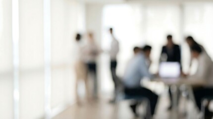 A blurry unfocused image depicts a group of people engaged in a meeting or discussion within a brightly lit modern office setting