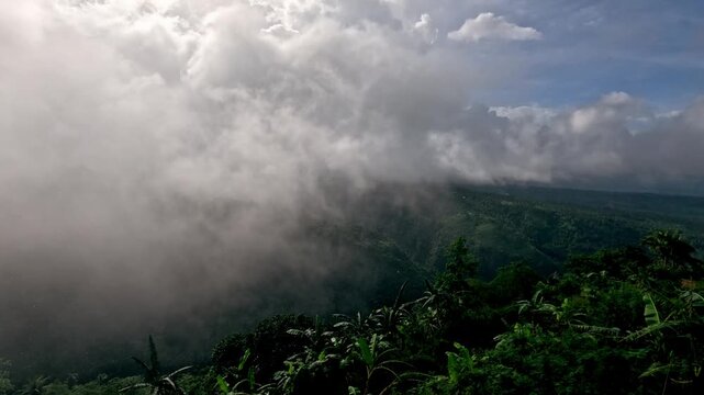 Hyperlapse of thunderous clouds rolling over a vast, mist-covered rainforest landscape on a rainy day during monsoon season in Pamplona, Negros Oriental, Philippines