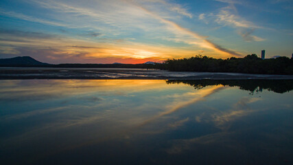 Under a radiant dusk sky, hues of orange and pink melt into tranquil waters. The lake captures...