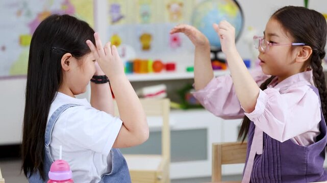 Two Young Asian Girls Playing Hand Clapping Games in a Kindergarten Classroom