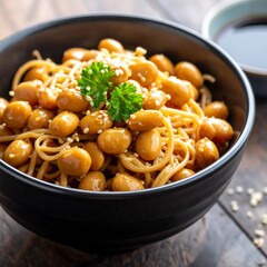 Bowl of glossy brown beans & noodles topped with parsley, on a dark wood table, with a blue sauce bowl