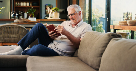 Reading, book and mature man on sofa with smile, calm and literature hobby on weekend rest. Free time, study and senior person in house with novel, relax and fantasy story on Saturday afternoon.