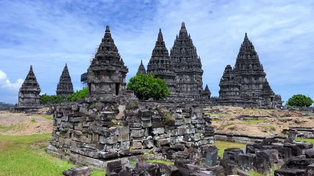 View of the ancient Prambanan Temple, a Hindu temple complex in Yogyakarta, Indonesia. The temple rises above the green foliage under a blue sky. The towers cast shadows on a sunny day. 4К
