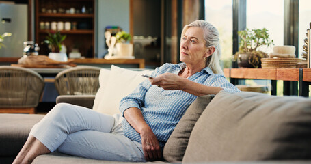 Obraz premium Senior woman, watching tv and remote on couch, search and click for movie choice in retirement at house. Elderly person, television show and relax on sofa with streaming, film or subscription in home