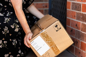 Woman by front door of home collecting box from online order delivery  
