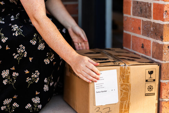 Woman by front door of home collecting box from online order delivery  