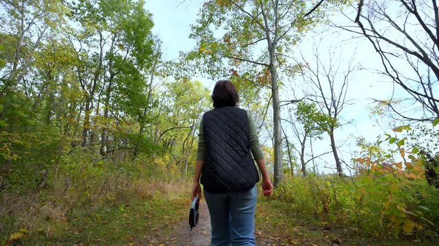 Woman enjoying a peaceful autumn walk in the forest, looking up at trees and taking in nature. Relaxed outdoor moment surrounded by colorful foliage.