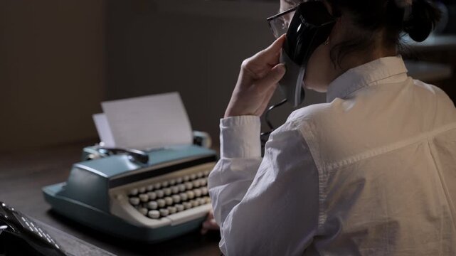 Person typing on a vintage typewriter and talking on a retro telephone. 