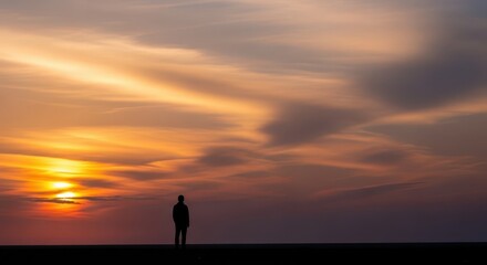 Fototapeta premium Solitary silhouette stands against a vibrant, fiery sunset sky.