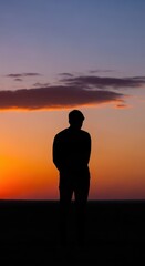 Fototapeta premium Solitary human figure stands silhouetted against a vivid twilight sky