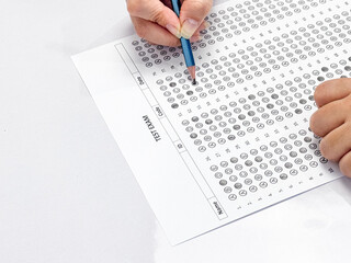 Student hand holding pencil filling out multiple choice answer sheet.1