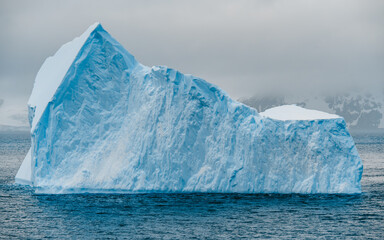 Massive Iceberg in Antarctica. Close Up View of Huge Piece of Ice Floating on Ocean. White and Blue Frozen Landscape Climate Change Calving Ice. © And They Travel