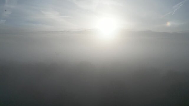 A foggy landscape with the sun barely visible through the mist.