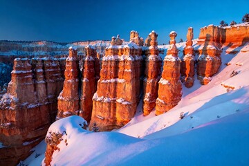 Snow-covered hoodoos in a red rock canyon at dawn