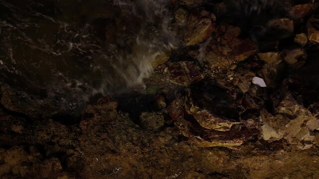B roll close up of fast flowing water over dark wet rocks at night showing white foam gray swirls and dramatic textures from an overhead perspective
