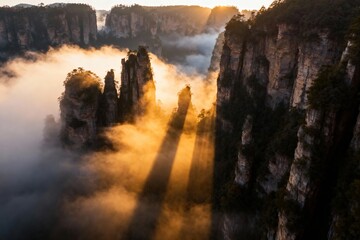 Sunlight piercing through mist over towering rock formations in a mountainous landscape