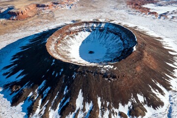 Aerial view of a snow-covered volcanic crater in a rugged desert landscape