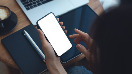 Mockup, Woman using mobile phone with blank white screen while online working on laptop at coffee...