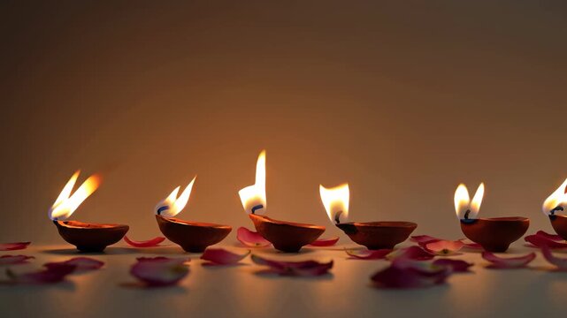 Diwali oil lamps flicker in sequence, adorned with rose petals. Celebrating the festival of lights with traditional diya and floral decoration.