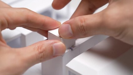 Close-up of hands carefully assembling a white architectural model or miniature structure. - Powered by Adobe