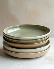 A stack of matte-finished ceramic plates in earthy tones (beige, sage green), minimal