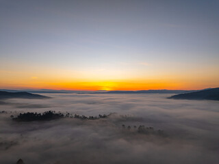 An aerial cinematic sunrise showcasing vibrant sky colors above a fog-covered valley, creating a serene and inspiring nature travel atmosphere. Brilliant Sunrise Painting the Sky Over the Valley