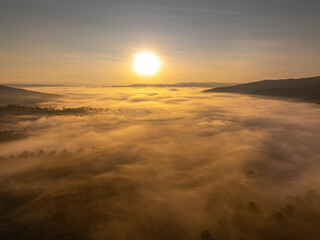 An aerial cinematic sunrise showcasing vibrant sky colors above a fog-covered valley, creating a serene and inspiring nature travel atmosphere. Brilliant Sunrise Painting the Sky Over the Valley