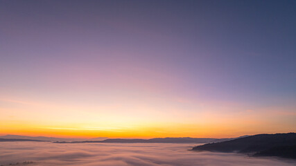 Obraz premium A stunning aerial landscape of sunrise over mountains wrapped in soft fog, perfect for travel, nature, and cinematic visual storytelling. Vibrant Sunrise Over a Tranquil Valley Wrapped in Morning Fog