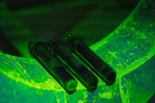 Threaded bolts under magnetic particle inspection with bright green fluorescent glow. An industrial non-destructive testing technique revealing surface defects using UV light for quality control
