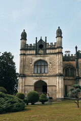 Obraz premium Castle facade rises over a manicured garden, featuring arched doorway, turrets, and weathered stonework, capturing historic architecture and a timeless estate atmosphere in tranquil grounds