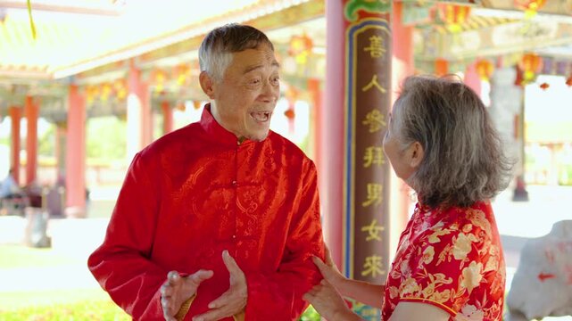 An elderly asian couple in bright cheongsams visits a colorful temple to pray, sharing laughter and stories while embracing the warmth of the Chinese New Year celebration with joy and love.