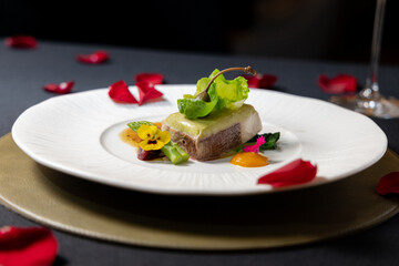 Elegant gourmet dish meticulously presented on a plate, featuring a tender piece of meat topped with vibrant garnish and complemented by delicate flower petals.