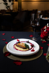 A gourmet dish artfully presented on a table, accompanied by a glass of wine and rose petals