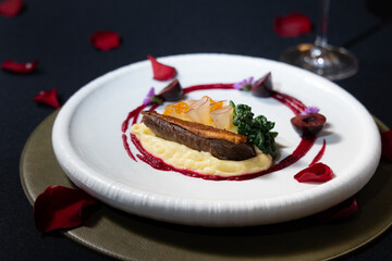 Gourmet dish artfully presented on a white plate with floral decoration and a glass of wine