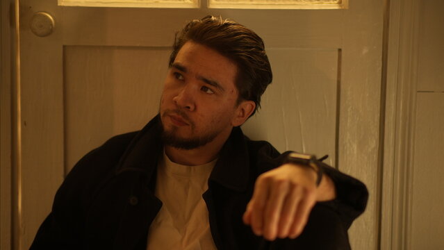 Moody portrait of a thoughtful man in a dark coat sitting in a dimly lit hallway at night. - Powered by Adobe