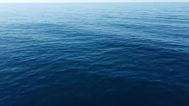 Aerial drone flight over deep blue open ocean water with gentle waves and horizon, calm sea surface background.