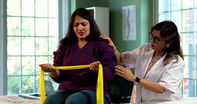 Indian lady physiotherapist examining shoulder pain of young female patient during detailed assessment in modern clinic, showing senior expertise in rotator cuff care and rehabilitation therapy