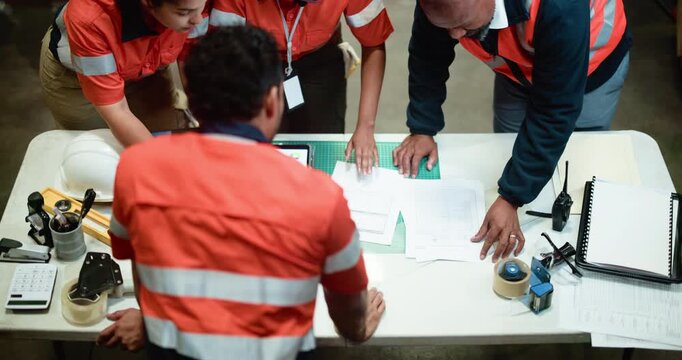 Group, construction and meeting with blueprint in warehouse above for supply chain expansion. Top view, people or team with documents for layout or building plan for storage improvement in depot