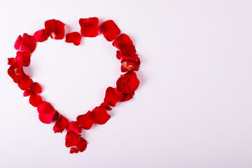 Overhead view of red rose petals arranged as heart shape with copy space on white background