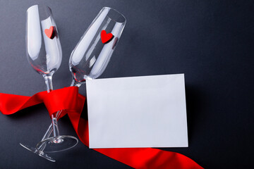 Champagne flutes tied with red ribbon by blank envelope isolated on gray background, copy space